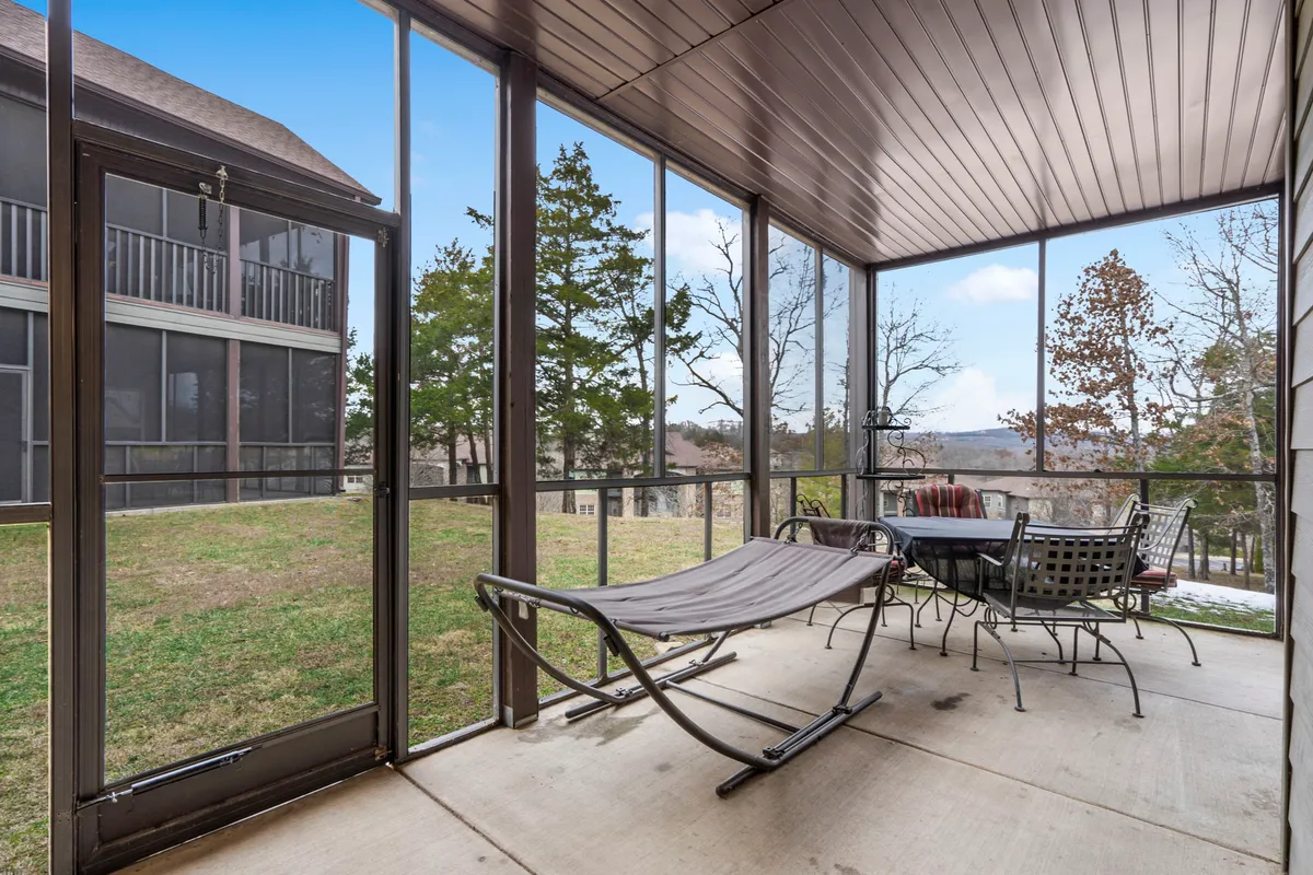 An inviting screened-in porch with a hammock prominently displayed, a dining table for group gatherings, and the porch's structure clearly showing the blend of indoor comfort and outdoor views. Natural light filters in, suggesting a tranquil spot for relaxing, entertaining, or enjoying the scenery regardless of weather.