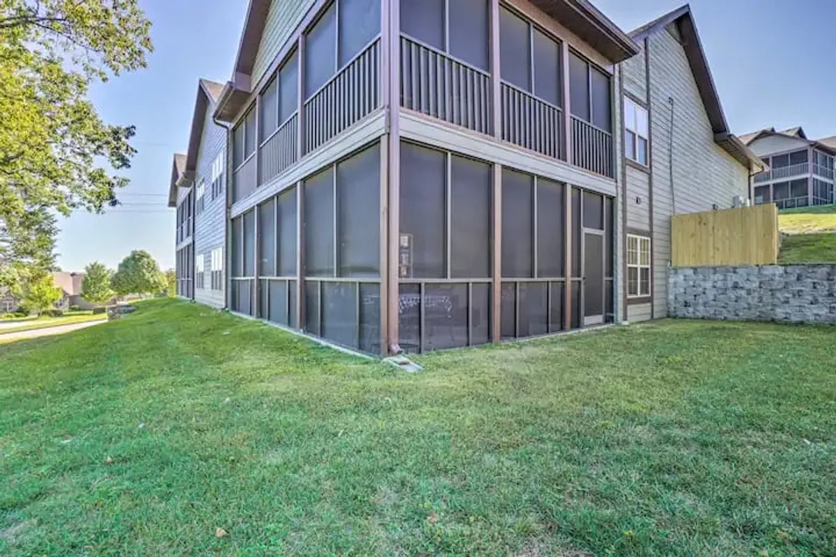 A clear exterior view of the screened-in porch with adjacent lawn area and building structure, evoking a sense of privacy and retreat. The scene suggests relaxation, socializing, and even opportunities for morning coffee or evening barbecues, with the porch as an essential transitional space.