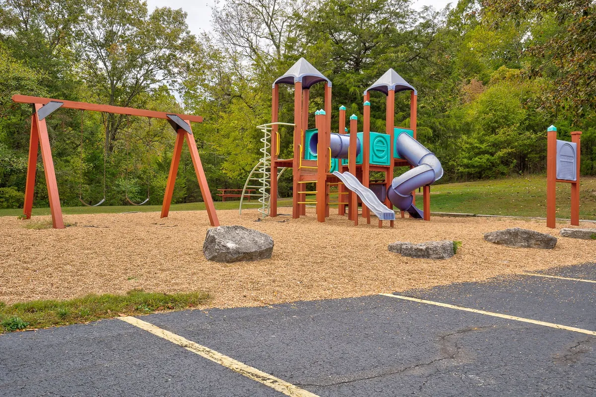 A colorful, modern playground with swings and climbing structures sits nestled in green space. Children play and families gather, demonstrating the community's family-friendly focus and opportunities for outdoor fun.