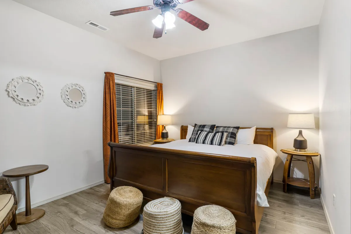This image features a well-appointed bedroom with a large bed, nightstand, lamps, window treatments, and mirrors. The overall ambiance is inviting and peaceful, suggesting a restful environment ideal for winding down after a busy day.