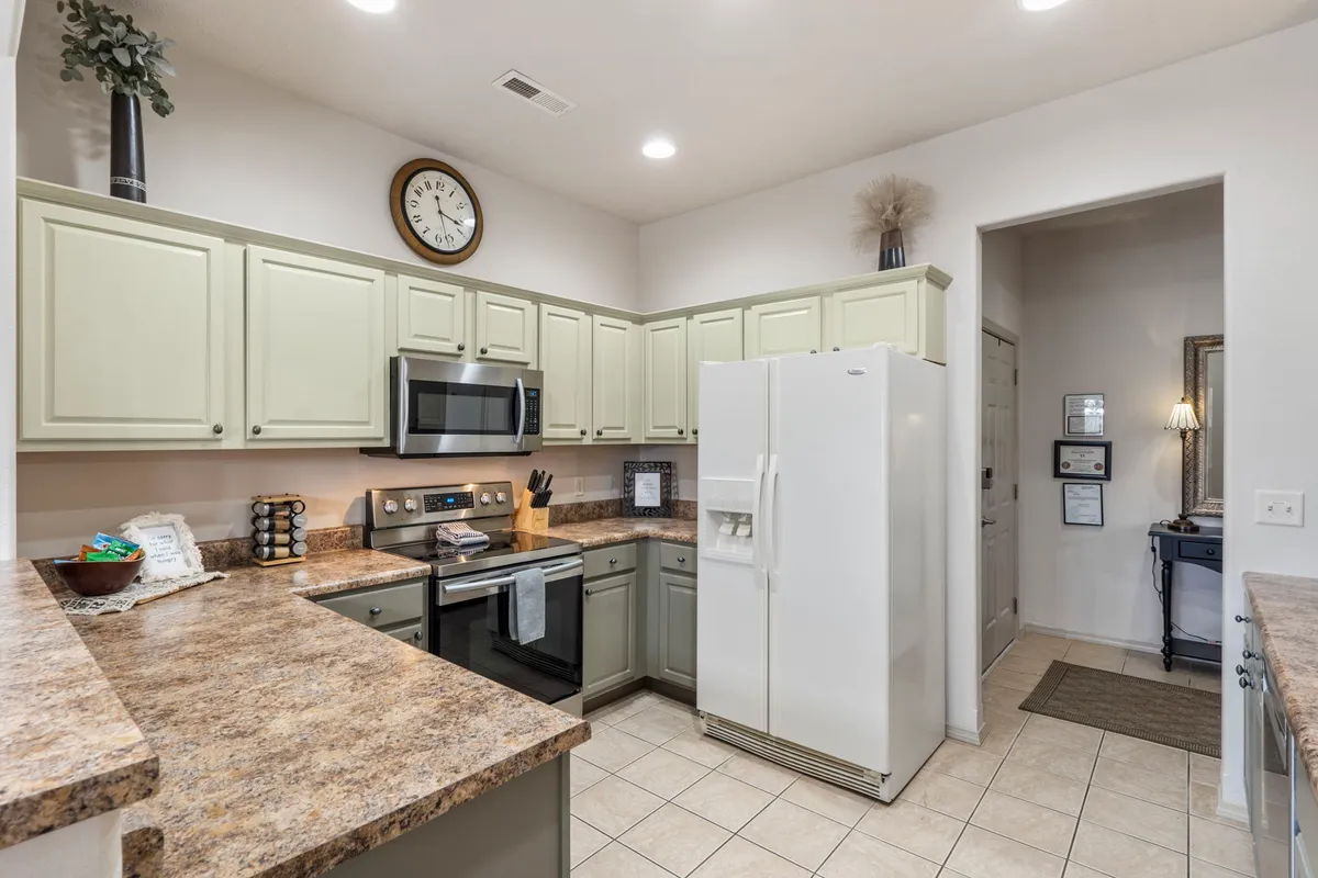 A bright and functional kitchen featuring a kitchen island, modern stainless steel appliances, and ample cabinetry. The white refrigerator and wall clock add a homey touch, while the layout is perfect for cooking, meal prep, and entertaining guests.