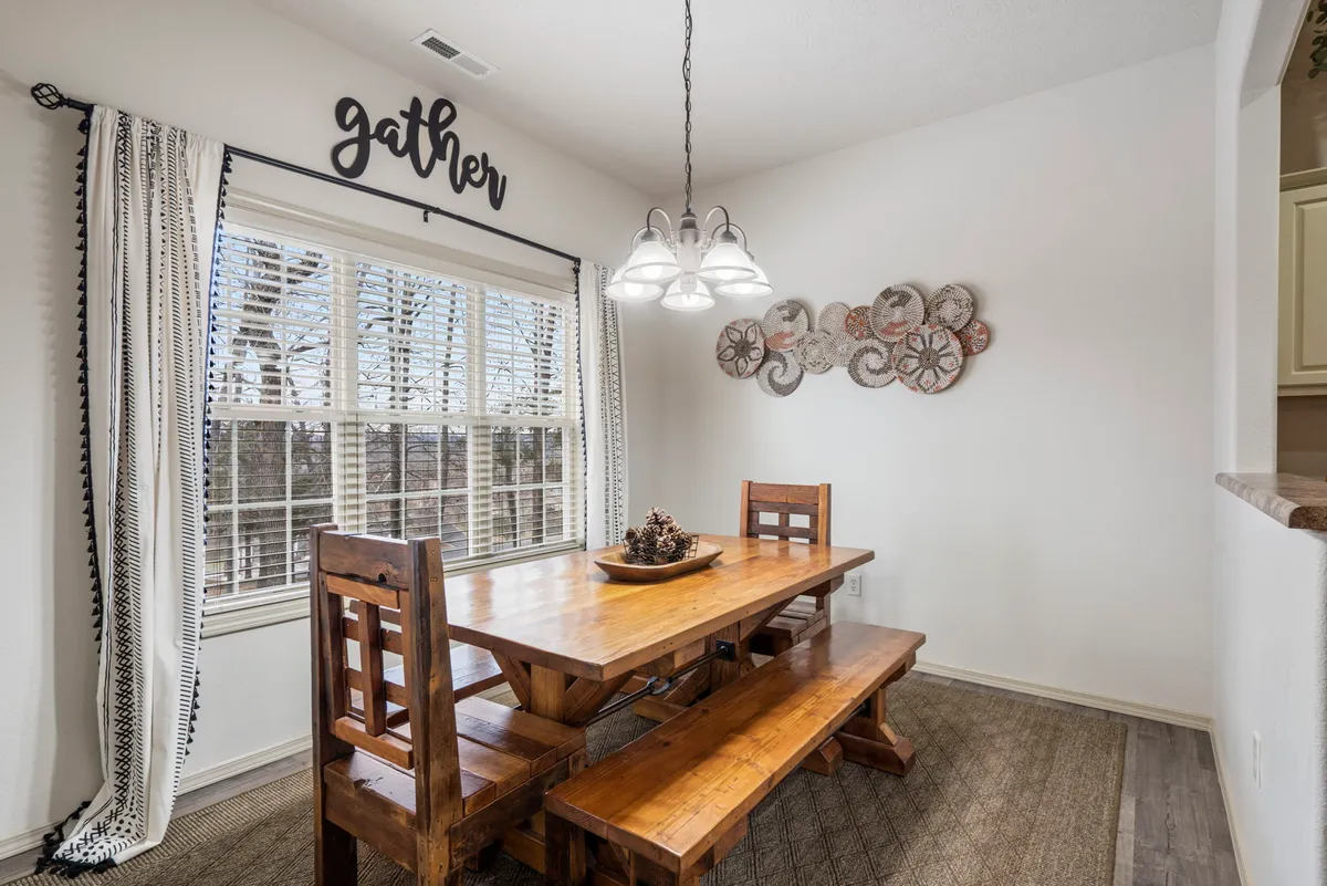 A welcoming dining area complete with a wooden dining table, matching chairs, elegant light fixture, and a window with soft curtains. The space is adorned with decorative wall art, creating a warm setting ideal for group meals or holiday gatherings.