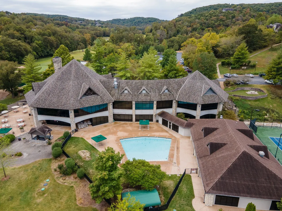 A vibrant exterior view of the resort’s expansive swimming pool surrounded by landscaped gardens, modern architecture, and visible tennis courts. The inviting setup includes lounge chairs and suggests active, leisurely pursuits.