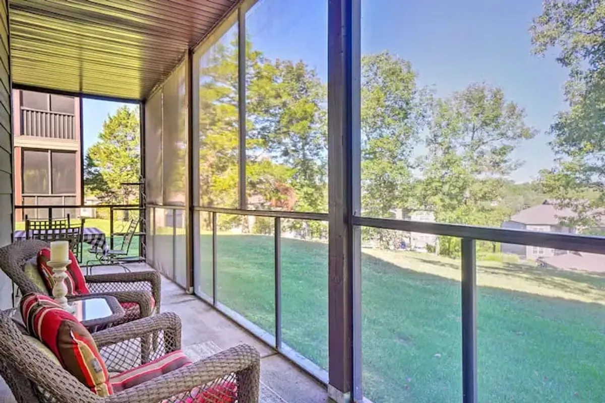 A serene exterior view of the screened porch, showcasing woven chairs set up for lounging, a lush green lawn, and trees in the background. The space feels open yet private, ideal for enjoying morning coffee, reading, or socializing outdoors while protected from the elements.