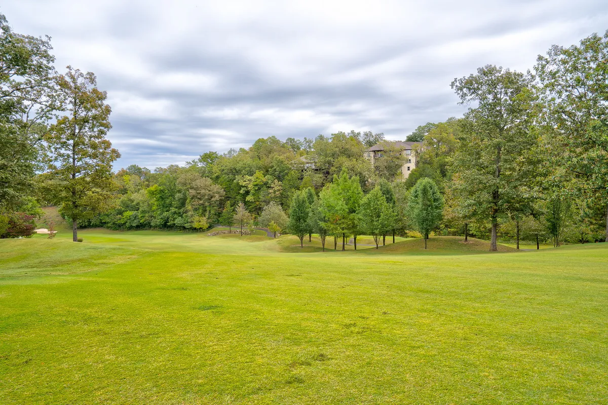 A serene expanses of green lawn bordered by clusters of trees and a distant building, evoking a calm and natural setting ideal for golf, picnicking, or peaceful strolls through the resort community.