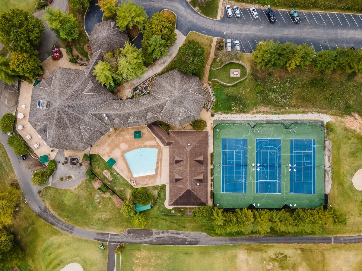 A large swimming pool with adjacent tennis courts, lush landscaped gardens, and the main resort building in the background. Families are seen swimming, playing tennis, and relaxing in the sun, embodying the energetic and leisurely aspects of resort life.